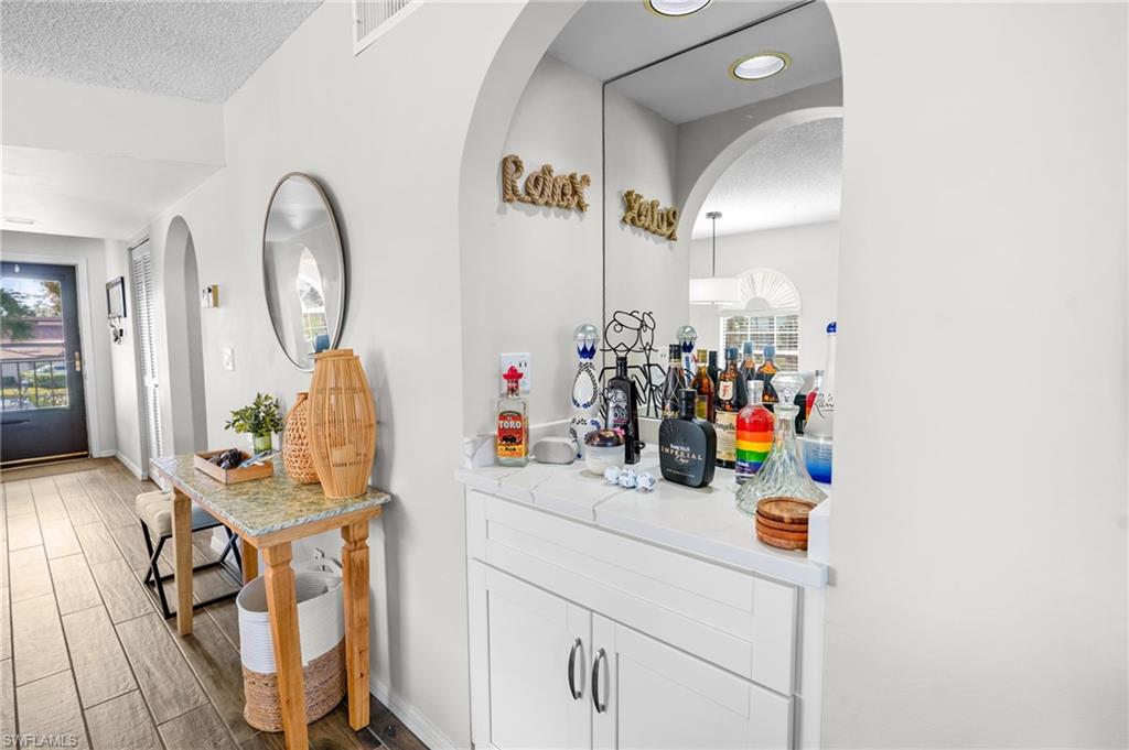 601 Augusta Boulevard, Unit 10 Naples, FL 34113 - Photo 17 of 27 Bar area featuring white cabinets, arched walkways, wood finish floors, and a textured ceiling