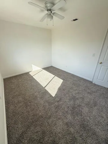 an empty room with a ceiling fan and carpet