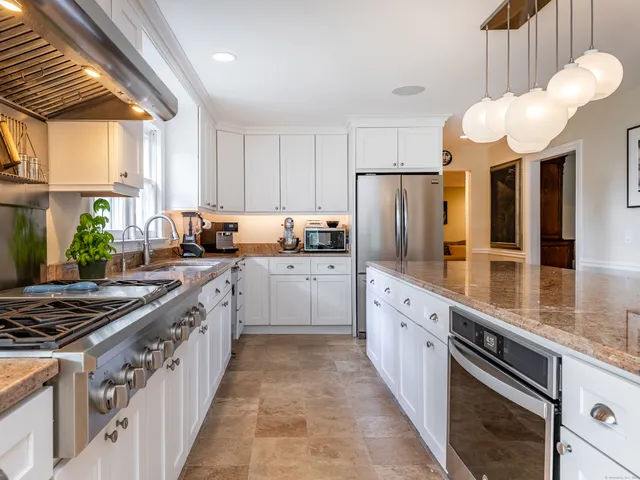 a white kitchen with stainless steel appliances granite countertop a stove a sink dishwasher and a refrigerator