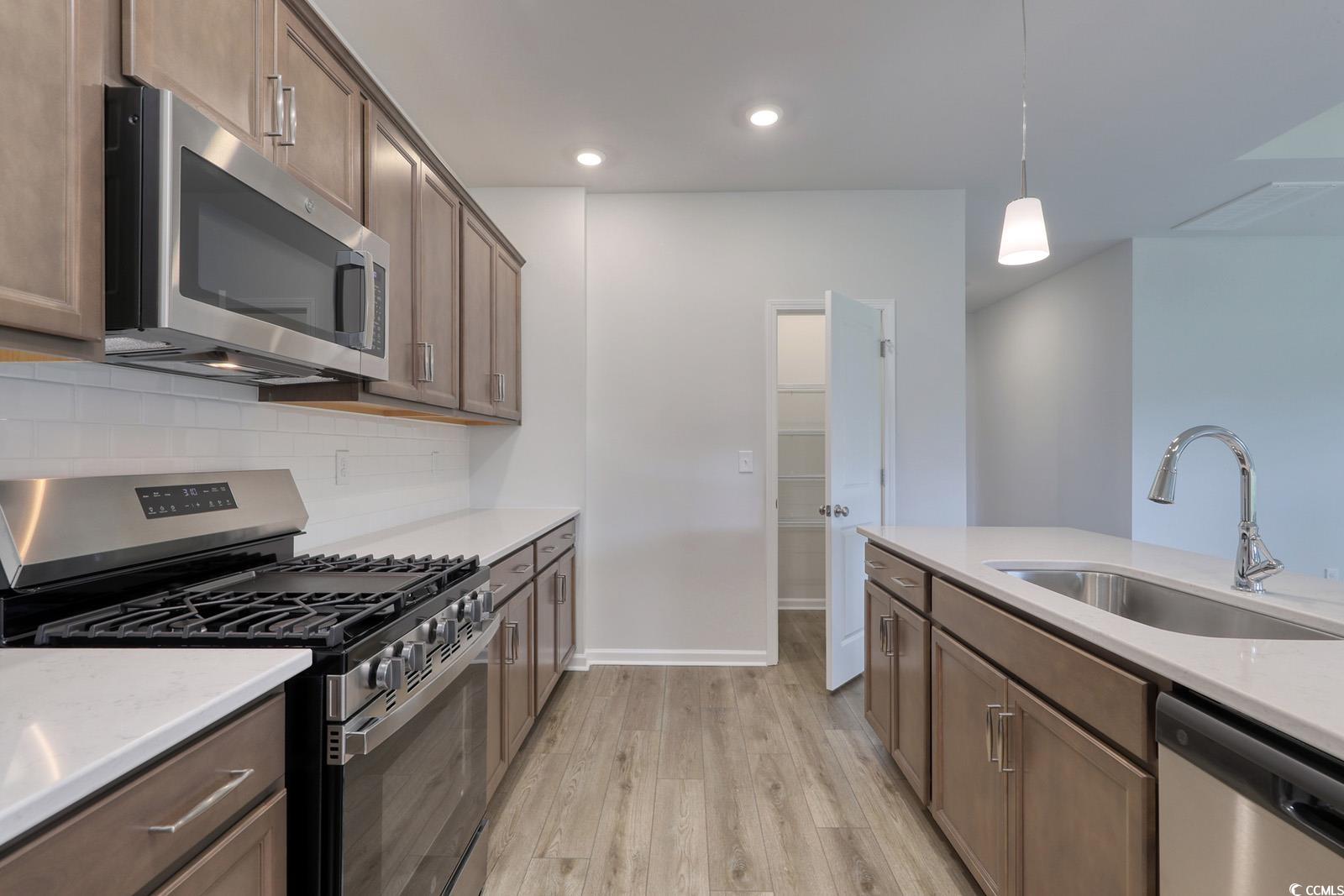311 Garden Grove Street Conway, SC 29526 - Photo 5 of 27 Kitchen featuring stainless steel appliances, decorative light fixtures, light wood-style flooring, light stone counters, and brown cabinetry