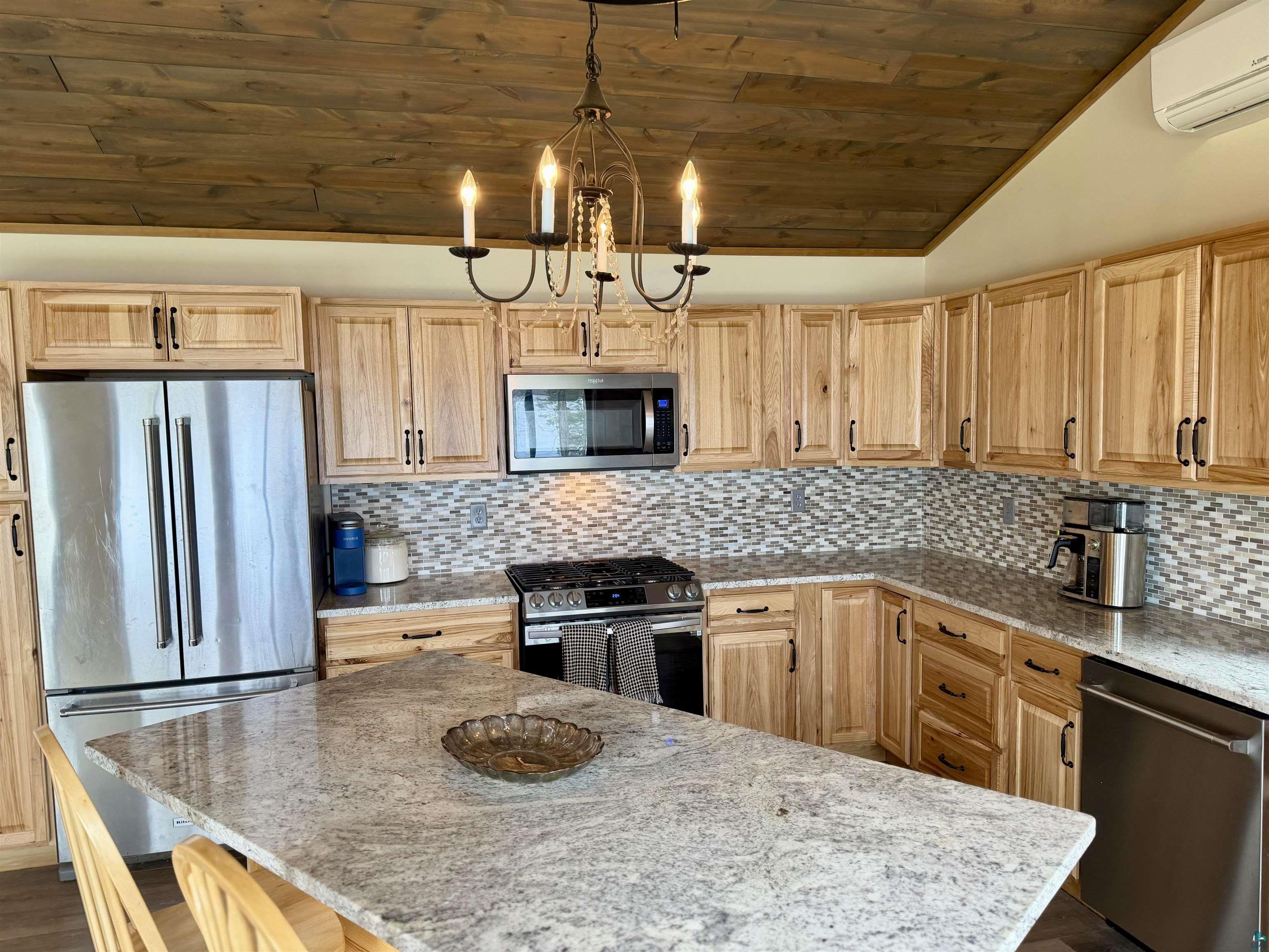 5274 Marble Lake Road Two Harbors, MN 55616 - Photo 25 of 79 Kitchen featuring wood-finish cabinetry, stainless steel appliances, a multi-tone tile backsplash, and a central island with a light-toned countertop