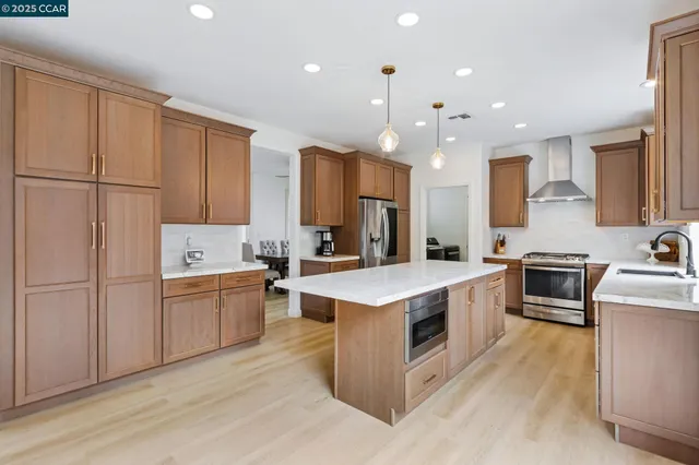 a large kitchen with stainless steel appliances granite countertop a stove a sink dishwasher and a refrigerator with wooden cabinets