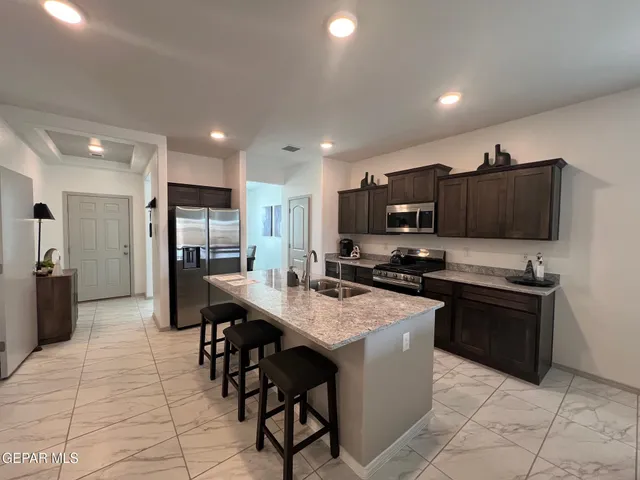 a kitchen with stainless steel appliances granite countertop a refrigerator a stove a sink a microwave and a dining table