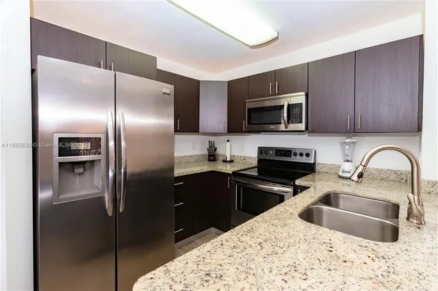 a kitchen with stainless steel appliances granite countertop a sink a stove a refrigerator a kitchen island with wooden cabinets