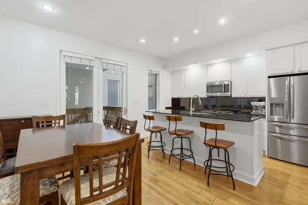 a kitchen with stainless steel appliances kitchen island granite countertop a refrigerator a stove a sink a dining table and chairs with wooden floor