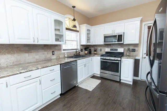 a kitchen with stainless steel appliances granite countertop white cabinets a sink a stove a refrigerator and microwave with wooden floor