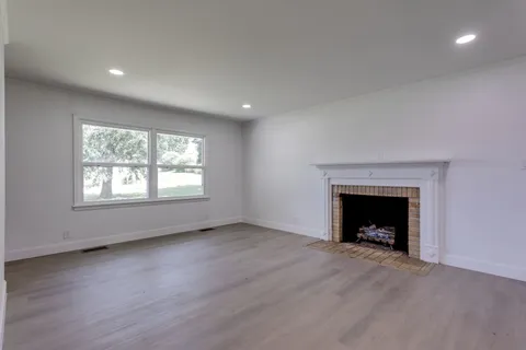 an empty room with wooden floor fireplace and windows