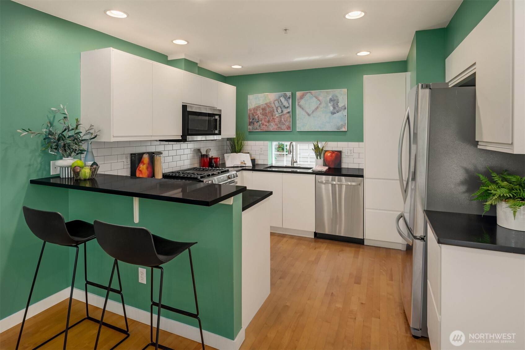 3302 West Government Way, Unit A Seattle, WA 98199 - Photo 15 of 32 a kitchen with stainless steel appliances kitchen island granite countertop a refrigerator a stove a sink dishwasher and white cabinets with wooden floor