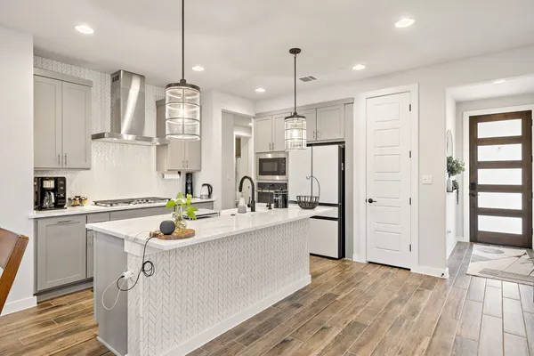 a kitchen with stainless steel appliances kitchen island a refrigerator a sink dishwasher a stove and white cabinets with wooden floor