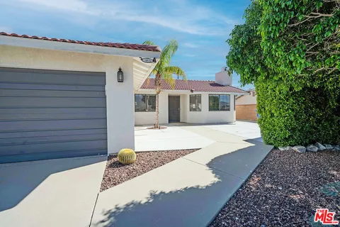 a view of a white house with a large window and flower plants