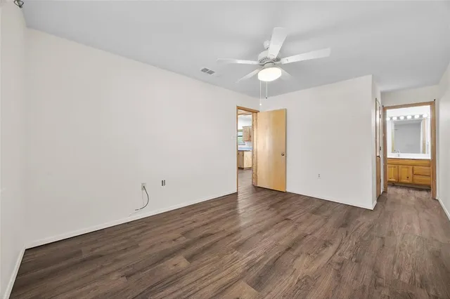 an empty room with wooden floor fan and windows