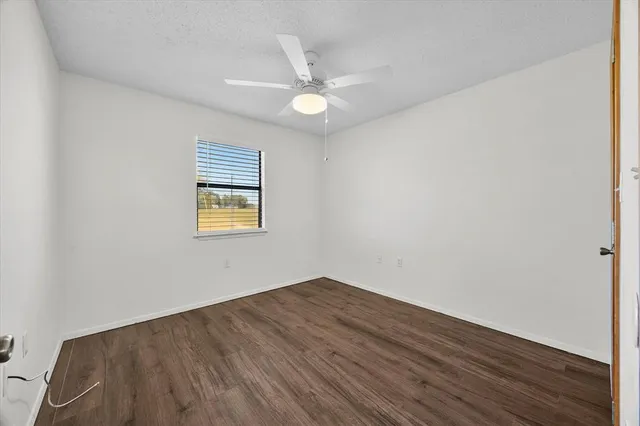 an empty room with wooden floor fan and windows
