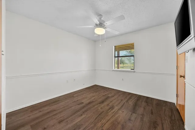 an empty room with wooden floor fan and windows