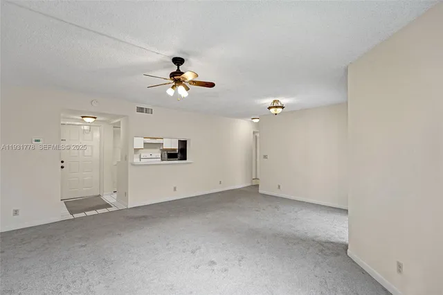 an empty room with chandelier fan and windows