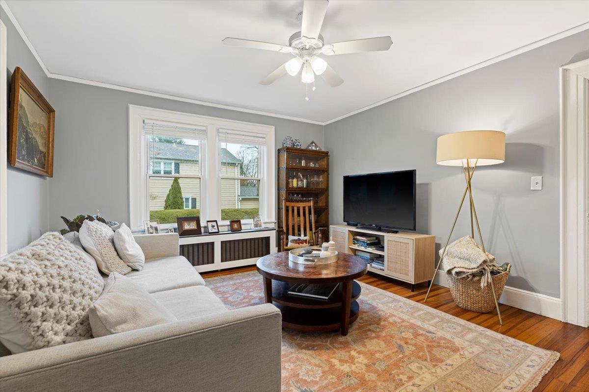 Living room featuring light wood-style flooring, crown molding, radiator heating unit, and a ceiling fan