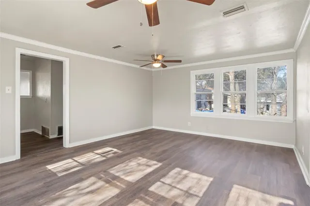 an empty room with wooden floor chandelier fan and windows
