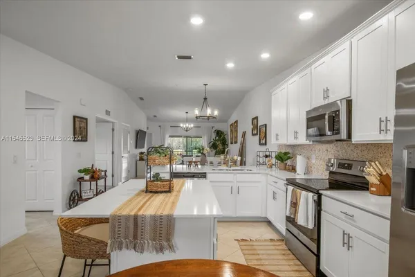 a kitchen with stainless steel appliances kitchen island granite countertop a refrigerator oven a sink dishwasher and white cabinets with wooden floor