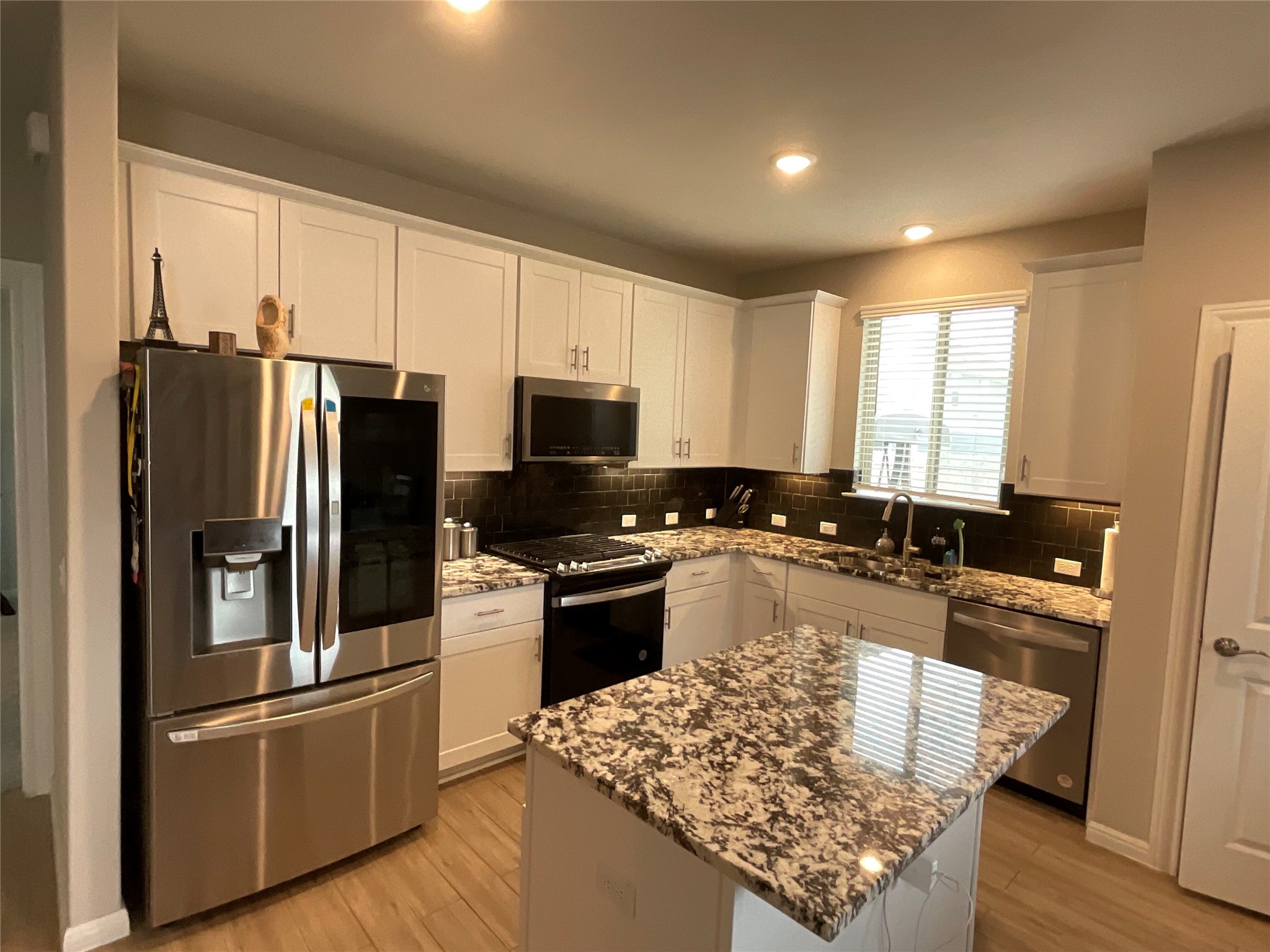 5425 Durango Pass Austin, TX 78724 - Photo 5 of 31 Kitchen with stainless steel appliances, white cabinetry, light stone countertops, light wood finished floors, and a center island