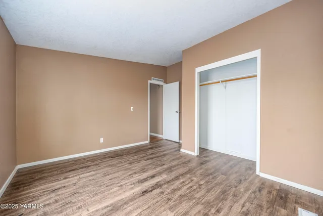 a view of an empty room with wooden floor and closet