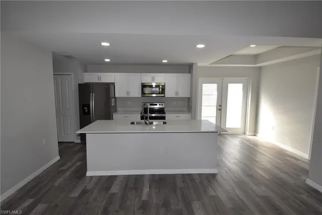 a living room with stainless steel appliances kitchen island granite countertop a refrigerator a sink a stove and a microwave with wooden floor