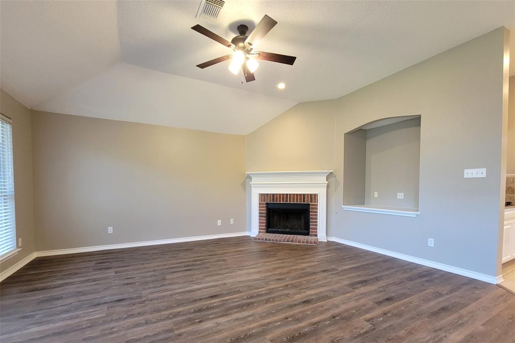 1604 Knoll Ridge Circle Corinth, TX 76210 - Photo 22 of 37 Spacious living area featuring wood-finish flooring, a brick-surround fireplace with a white mantel, and a vaulted ceiling with a ceiling fan
