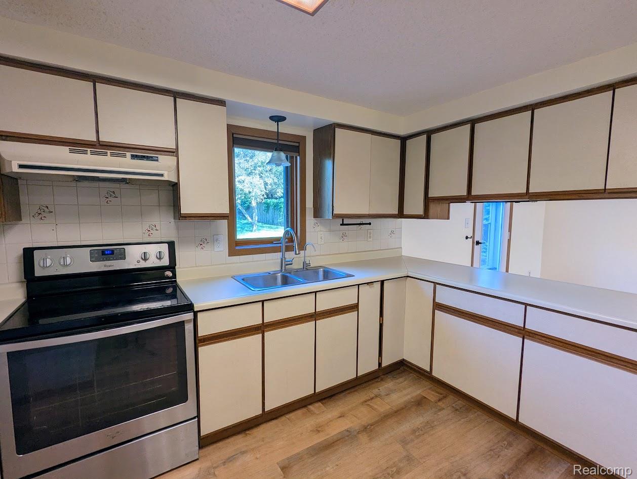 2316 Crescent Lake Road Waterford, MI 48329 - Photo 12 of 17 Kitchen featuring wood-finish flooring, stainless steel range, double basin sink, white cabinetry with wood trim, and a window overlooking exterior greenery