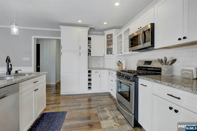 a kitchen with stainless steel appliances granite countertop a sink and a stove top oven with white cabinets
