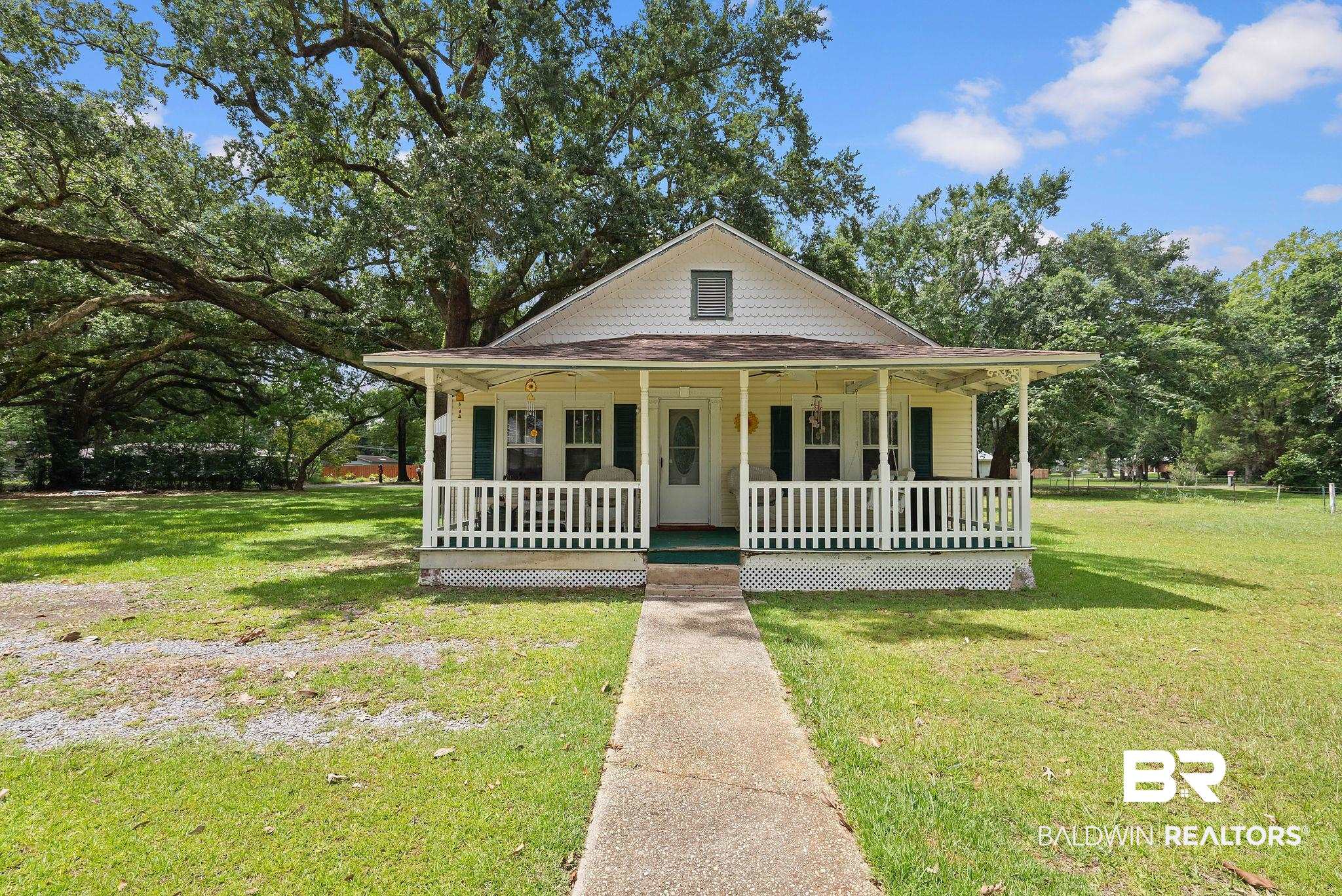615 West Section Avenue Foley, AL 36535 - Photo 1 of 40 Cottage-style residence featuring a covered front porch with white railing, light yellow siding, and dark green louvered shutters