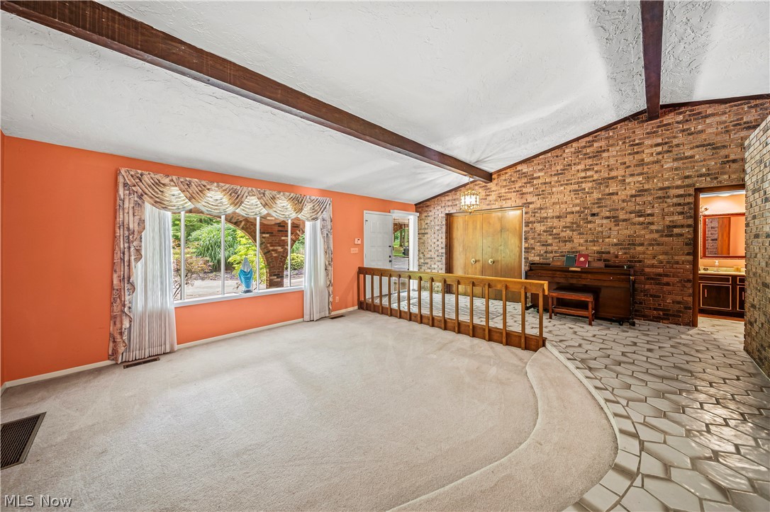 12200 Caves Road Chesterland, OH 44026 - Photo 10 of 43 Unfurnished living room with carpet flooring, brick wall, and lofted ceiling with beams