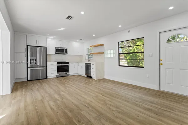 an empty room with stainless steel appliances wooden floor and windows
