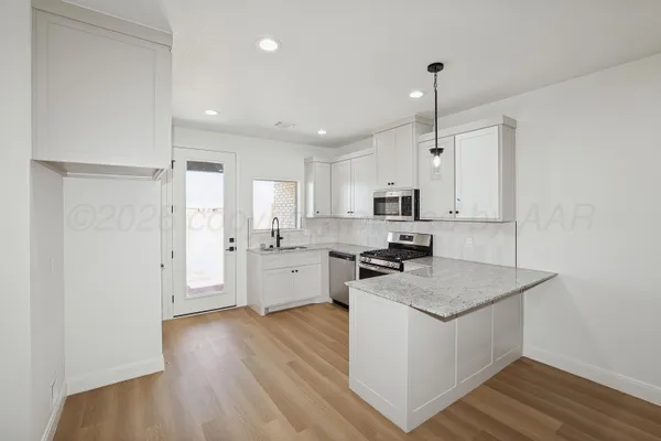 a kitchen with stainless steel appliances a refrigerator a sink dishwasher a stove and white cabinets with wooden floor