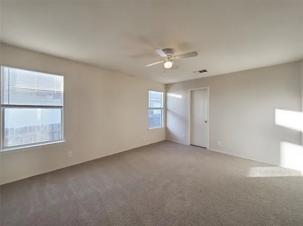 an empty room with chandelier fan and windows
