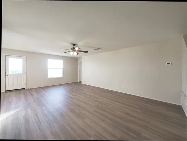 an empty room with wooden floor ceiling fan and windows