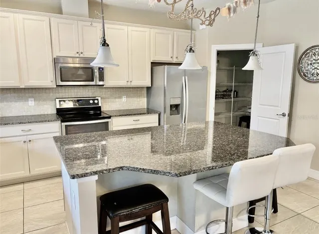 a kitchen with stainless steel appliances granite countertop a stove top oven a refrigerator a sink and white cabinets