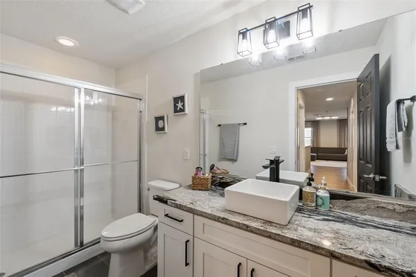 a bathroom with a granite countertop sink a toilet a mirror and shower
