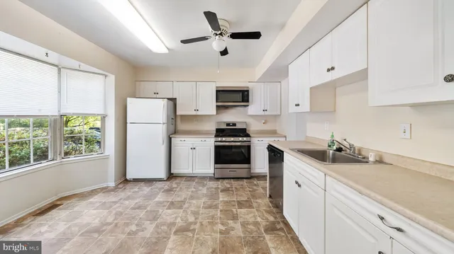 a kitchen with granite countertop a refrigerator a sink a stove and white cabinets