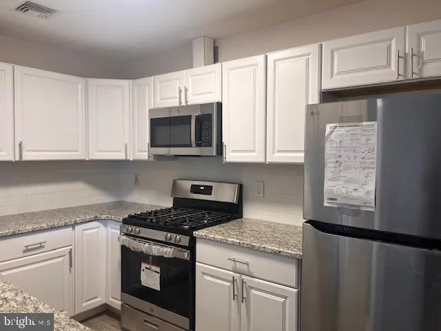 a kitchen with stainless steel appliances granite countertop white cabinets granite counter tops and a window