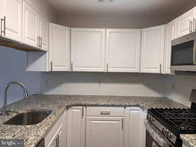 a kitchen with granite countertop a sink dishwasher a stove and cabinets