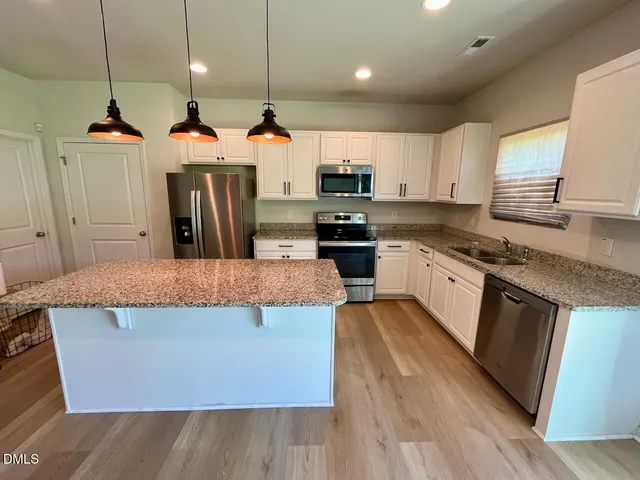 a kitchen with stainless steel appliances granite countertop a stove a sink a refrigerator and white cabinets with wooden floor