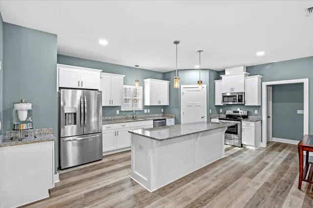 a large kitchen with stainless steel appliances kitchen island granite countertop a refrigerator a stove a sink and white cabinets with wooden floor