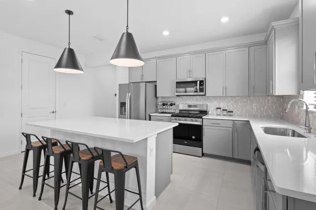 a kitchen with kitchen island stainless steel appliances a dining table chairs sink and cabinets