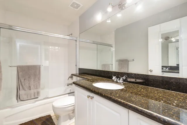 a bathroom with a granite countertop sink a mirror a toilet and shower