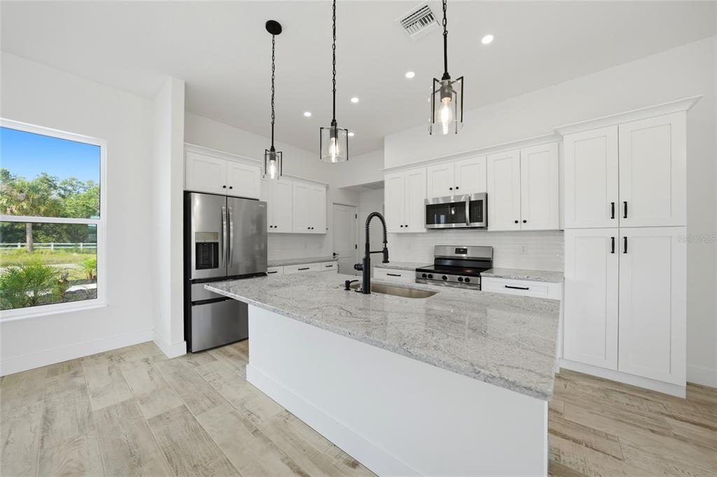 8846 Southwest Liverpool Road Arcadia, FL 34269 - Photo 9 of 49 a kitchen with stainless steel appliances granite countertop a sink a stove a refrigerator a center island with wooden floor and cabinets