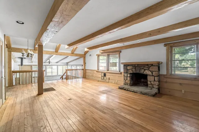 a view of an empty room with wooden floor fireplace and a window