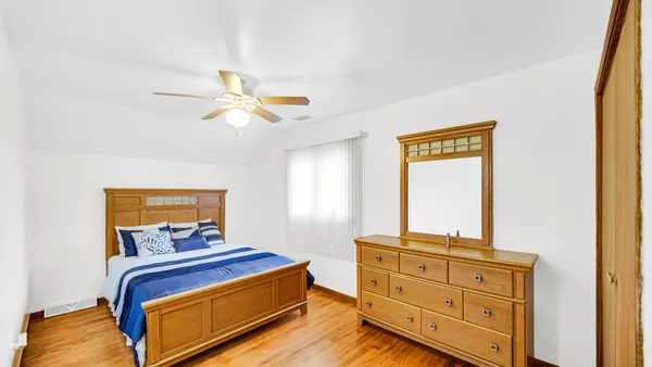 a bedroom with a bed and a dresser with wooden floor