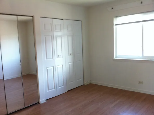 an empty room with wooden floor closet and windows