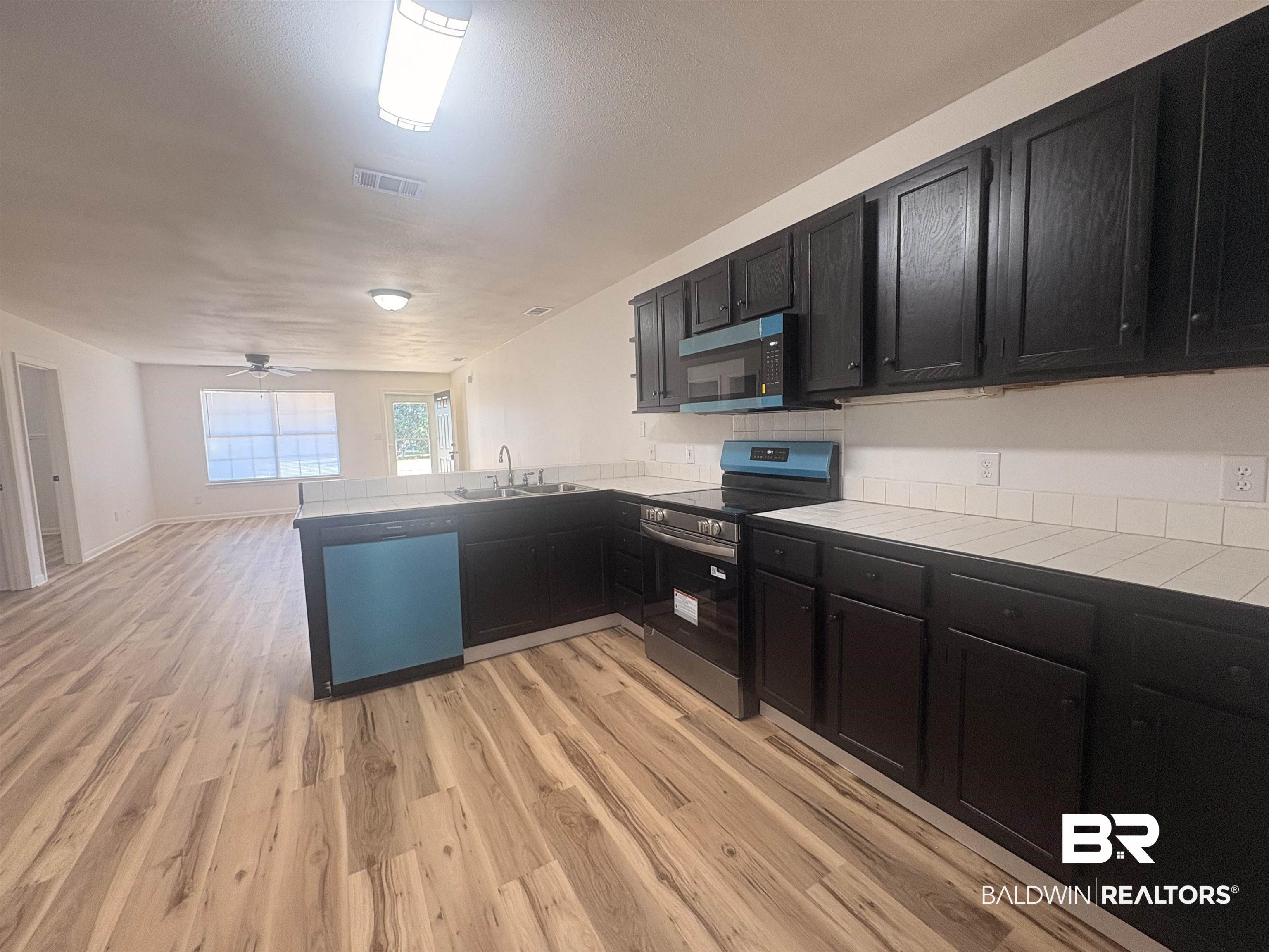 109-111 North Beech Street, Unit A & B Foley, AL 36535 - Photo 5 of 16 Kitchen featuring dark cabinets, tile counters, stainless steel appliances, light wood finished floors, and a peninsula