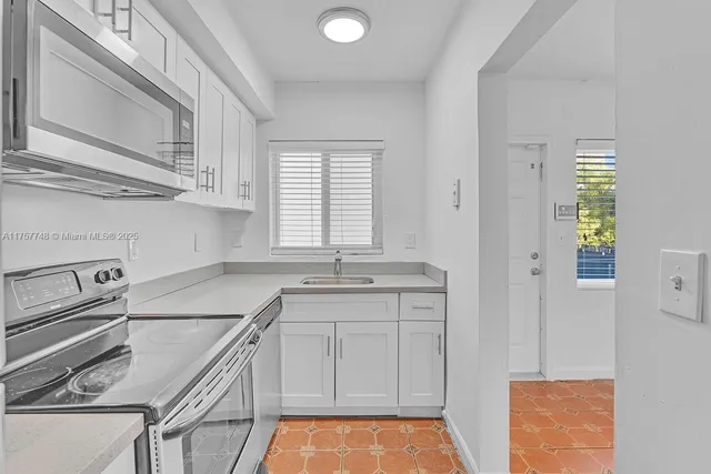 a kitchen with granite countertop a sink stainless steel appliances white cabinets and a window