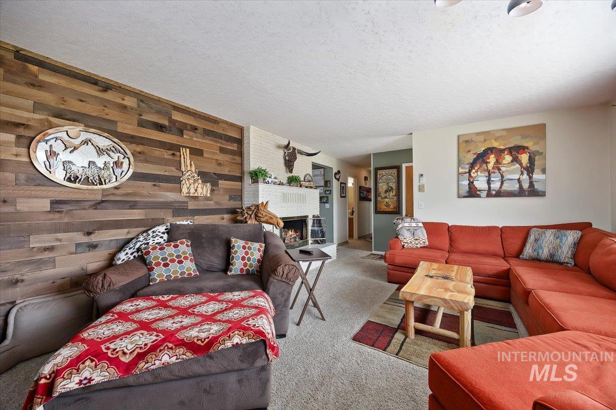1301 A Street Rupert, ID 83350 - Photo 7 of 45 Carpeted living room featuring a textured ceiling, a lit fireplace, and wooden walls