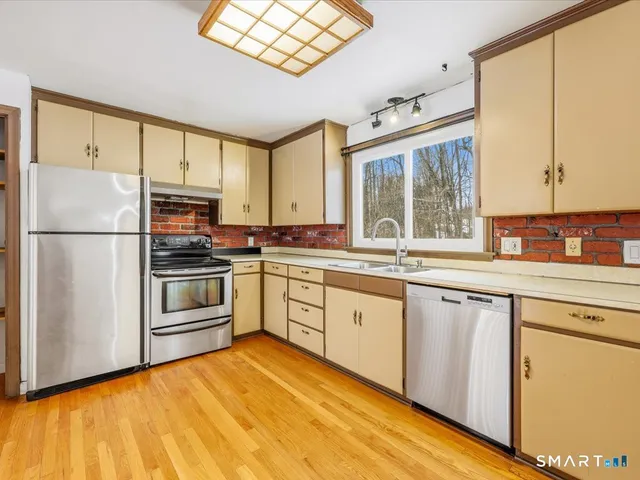 a kitchen with granite countertop a refrigerator a sink dishwasher a stove and white cabinets with wooden floor